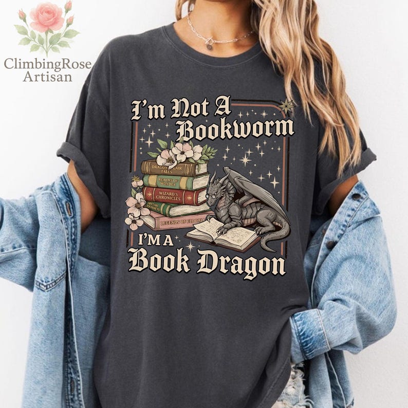 Pode incluir: Camiseta cinza escuro com o texto "I'm Not A Bookworm, I'm A Book Dragon." O gr&aacute;fico apresenta uma pilha de livros, flores e um drag&atilde;o lendo. A camiseta tem mangas enroladas.