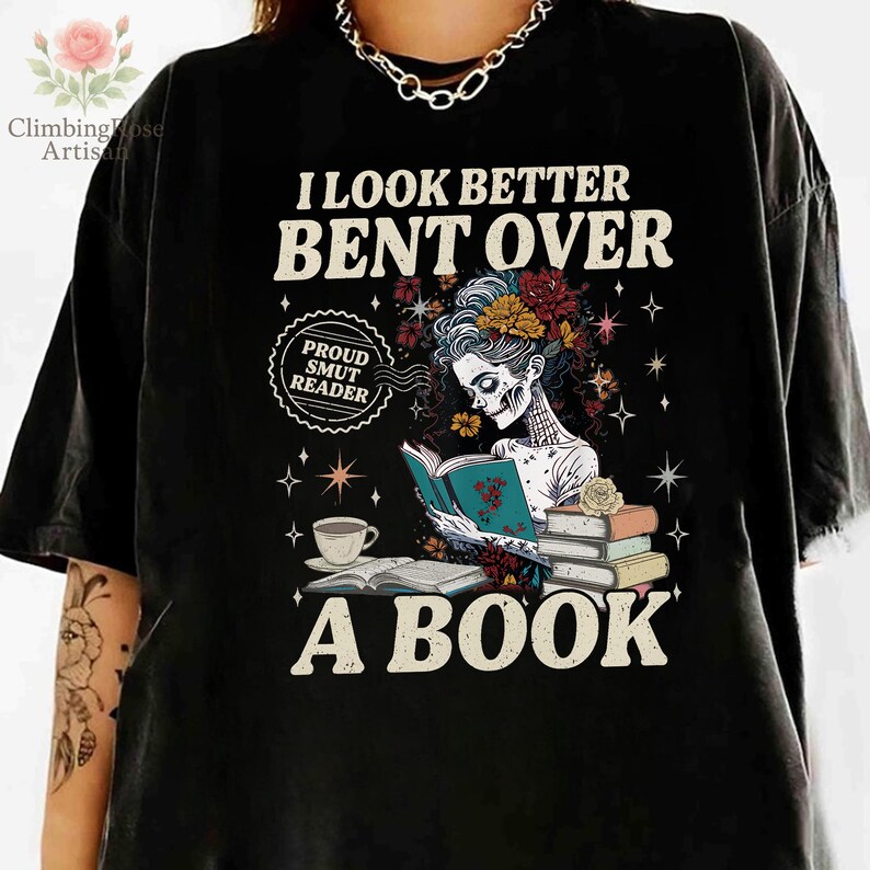 May include: Black t-shirt with the text "I LOOK BETTER BENT OVER A BOOK". The shirt features a skeleton woman reading a book, with floral and star graphics. A coffee cup and books are also shown.