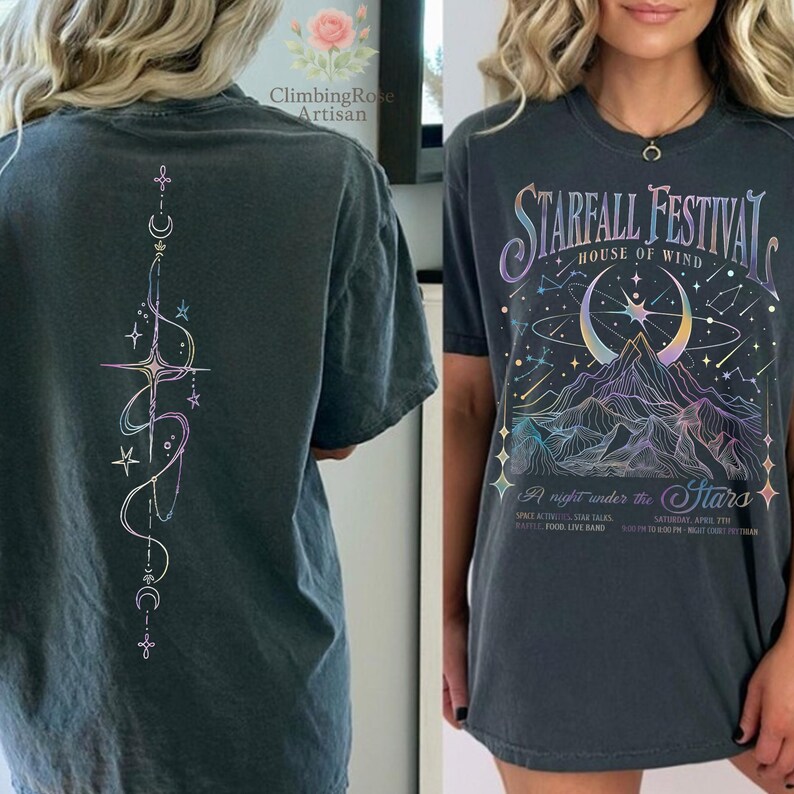 May include: Dark gray t-shirt featuring a celestial design on the back and a "Starfall Festival" graphic on the front. The front design includes a mountain range, crescent moon, and stars in iridescent colors. The back features a vertical design with stars and moons.