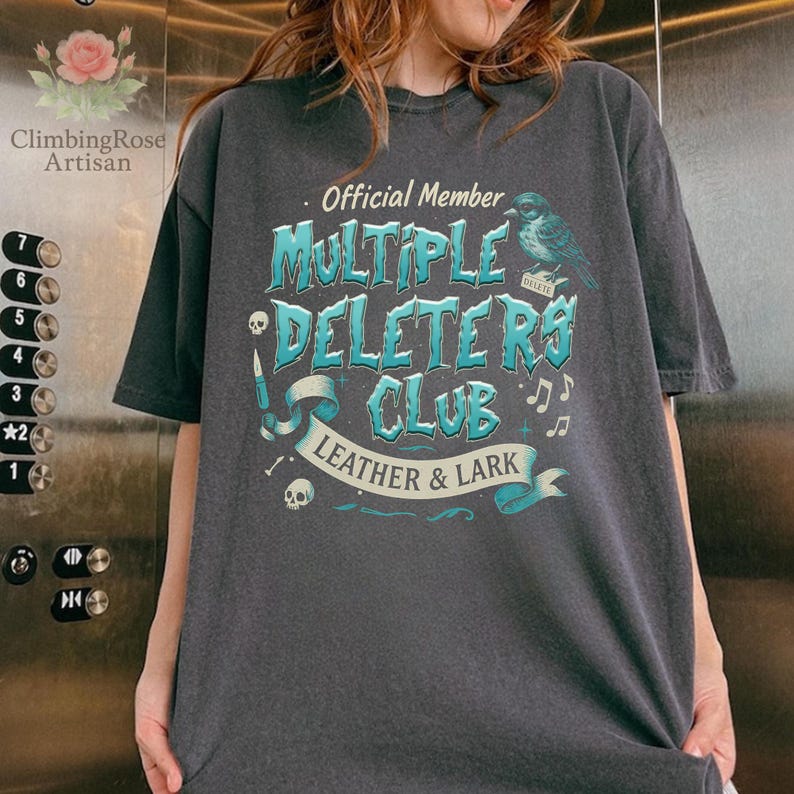 May include: A dark gray t-shirt with a blue and white graphic design that says "Official Member Multiple Deleters Club Leather & Lark".