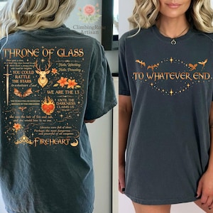May include: Dark gray t-shirts with fantasy-themed text and graphics. One shirt features the text "THRONE OF GLASS" and other text with a deer, heart, and floral design. The other shirt says "TO WHATEVER END" with bats and stars.
