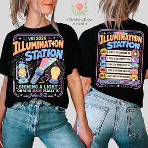 Pu&ograve; includere: T-shirt nera con un design grafico colorato. La parte anteriore presenta il testo "VBS 2026 ILLUMINATION STATION" con illustrazioni di una lanterna, una torcia e una lampadina. Il retro mostra "ILLUMINATION STATION" e un elenco di versetti biblici.