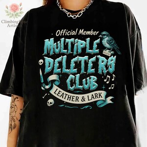 May include: Black t-shirt with a blue and white graphic design that says "Official Member Multiple Deleters Club Leather & Lark". The graphic also includes a skull, a knife, a bird, and musical notes.