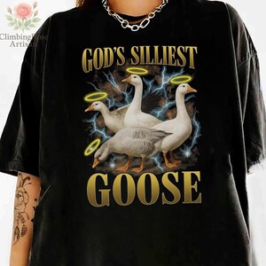 May include: Black t-shirt featuring a graphic of three geese with halos, set against a backdrop of lightning bolts. The text "GOD'S SILLIEST GOOSE" is displayed in gold lettering, creating a humorous and eye-catching design.