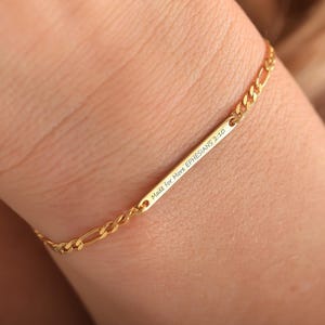 May include: A gold bracelet featuring a chain link design and a rectangular bar. The bar is engraved with the text "Made for More EPHESIANS 2:10". The bracelet is worn on a wrist.
