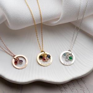 May include: Three personalized necklaces with circular pendants and gemstone clusters. The necklaces are in rose gold, gold, and silver. The rose gold necklace has the text "I LOVE YOU". The gold necklace has the names "Alex + Emily". The silver necklace has the date "05.09.2023".