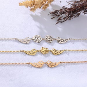 Op de afbeelding: Drie delicate armbanden. De bovenste armband is zilverkleurig, met een roos en een bloem tussen twee vleugelbedels. De middelste armband is goudkleurig, met een bloem tussen twee vleugelbedels. De onderste armband is roségoudkleurig, met twee vleugelbedels.