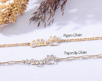 May include: Two gold-colored name bracelets. One says "Chloe" with a paw print charm, the other says "Maya" with a paw print charm. The top bracelet has a Figaro chain, and the bottom bracelet has a paperclip chain.