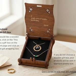 Puede incluir: Caja de regalo de joyer&iacute;a de madera abierta, que revela dos collares de oro con piedras preciosas. La caja est&aacute; grabada con "I wish you a happy birthday" y "Mom". La caja est&aacute; sobre una superficie clara, con un anillo de oro visible.