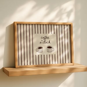 May include: A framed print featuring a beige background with vertical brown stripes. The print includes the text "coffee o'clock" and two coffee cup illustrations. The frame is made of light brown wood, and the print is displayed on a wooden shelf.