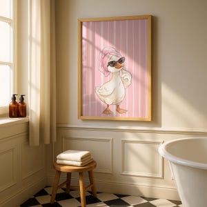 May include: A framed wall art print featuring a white duck wearing a pink towel wrapped around its head and black sunglasses. The duck is positioned against a background of vertical pink and white stripes, rendered in a soft illustration style.