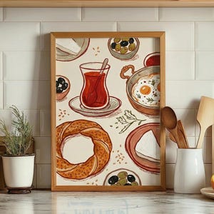 May include: A framed print featuring a watercolor illustration of a Turkish breakfast. The artwork includes a glass of tea, fried eggs, olives, cheese, and a bagel. The frame is made of wood and is displayed on a kitchen counter.