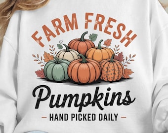 May include: White sweatshirt with a graphic of six pumpkins in shades of orange, green, and cream, with the words "FARM FRESH" and "Pumpkins - HAND PICKED DAILY" in brown and black lettering. Autumn-themed design.