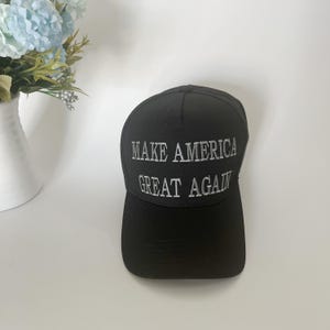May include: Black baseball cap with the embroidered text "MAKE AMERICA GREAT AGAIN" in white. The cap is made of a durable fabric and features a curved brim. The hat is a classic style, suitable for everyday wear.