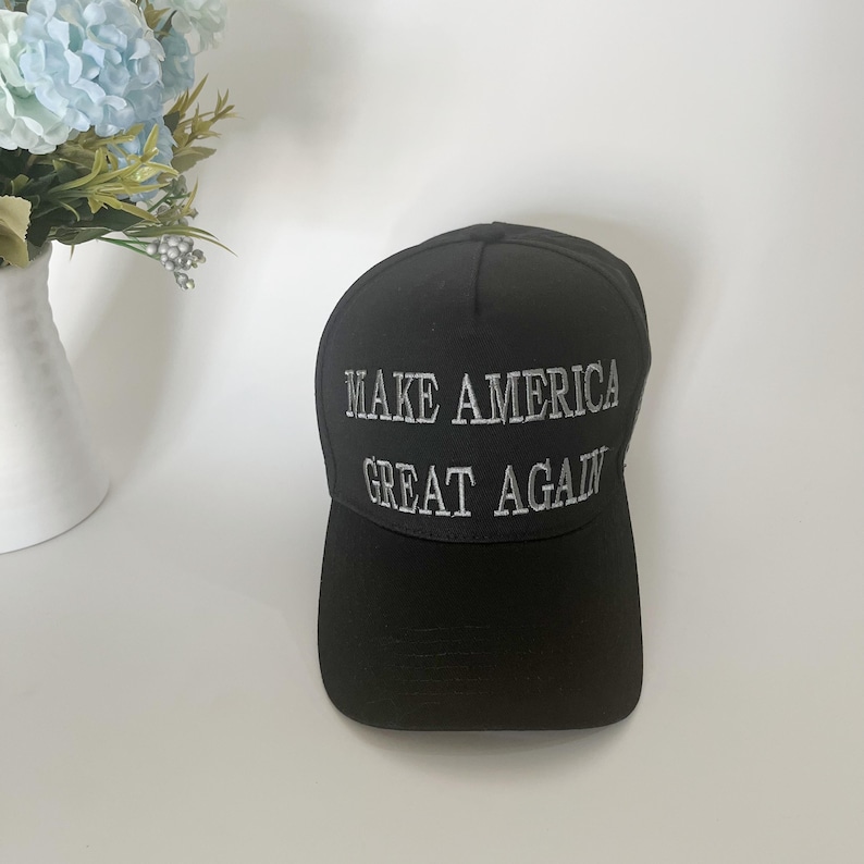 May include: Black baseball cap with the embroidered text "MAKE AMERICA GREAT AGAIN" in white. The cap is made of a durable fabric and features a curved brim. The hat is a classic style, suitable for everyday wear.