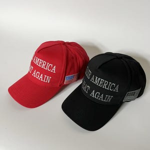 May include: Two baseball caps, one red and one black. Both caps have the phrase "MAKE AMERICA GREAT AGAIN" embroidered in white. A small American flag patch is on the side of each cap.