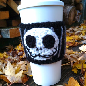 Puede incluir: Taza de viaje blanca con un forro de punto de crochet negro y gris con un rostro de Jack Skellington blanco y negro. El forro tiene un patr&oacute;n a rayas.