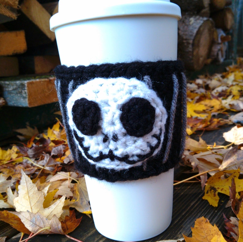Puede incluir: Taza de viaje blanca con un forro de punto de crochet negro y gris con un rostro de Jack Skellington blanco y negro. El forro tiene un patr&oacute;n a rayas.