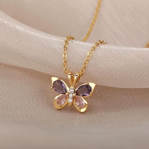 Peut inclure: Un collier en chaîne dorée avec un pendentif en forme de papillon. Le papillon est orné de pierres précieuses violettes et roses et de strass transparents.