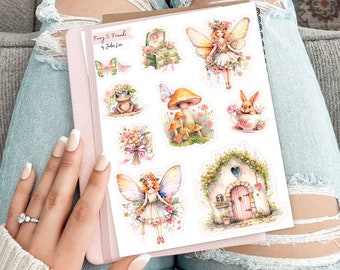 May include: A sticker sheet titled Fairy & Friends by Julie Lee featuring illustrations of fairies, a frog with a flower crown, a mushroom, a rabbit in a teacup, a bouquet of flowers, and a small cottage with a pink door and heart-shaped window.