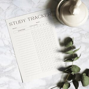 Op de afbeelding: Een zwart-witte printbare studietracker met de tekst "STUDY TRACKER" bovenaan. De tracker heeft kolommen voor "Maand", "Hoofdstukken", "Week" en "Aantal keer herzien". Er zijn zeven kolommen voor de week en 30 rijen voor hoofdstukken.