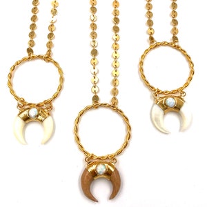 May include: Three gold necklaces with crescent moon pendants. Each pendant features a different material: white, wood, and white with a gold accent. Each pendant has a small opal-like stone in the center.