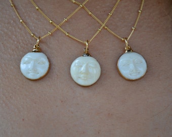 May include: Three gold necklaces with white moon pendants featuring a carved face design. Each pendant is about 1 inch in diameter.