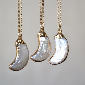 May include: Three gold-plated necklaces with crescent-shaped pendants. The pendants are white and have a gold-colored trim. The necklaces hang from delicate gold chains, creating an elegant and minimalist design.
