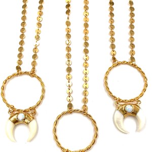 May include: Three gold necklaces with a crescent moon pendant. The pendants are made of wood, bone, and opal. The necklaces are made of gold chain and coin links.