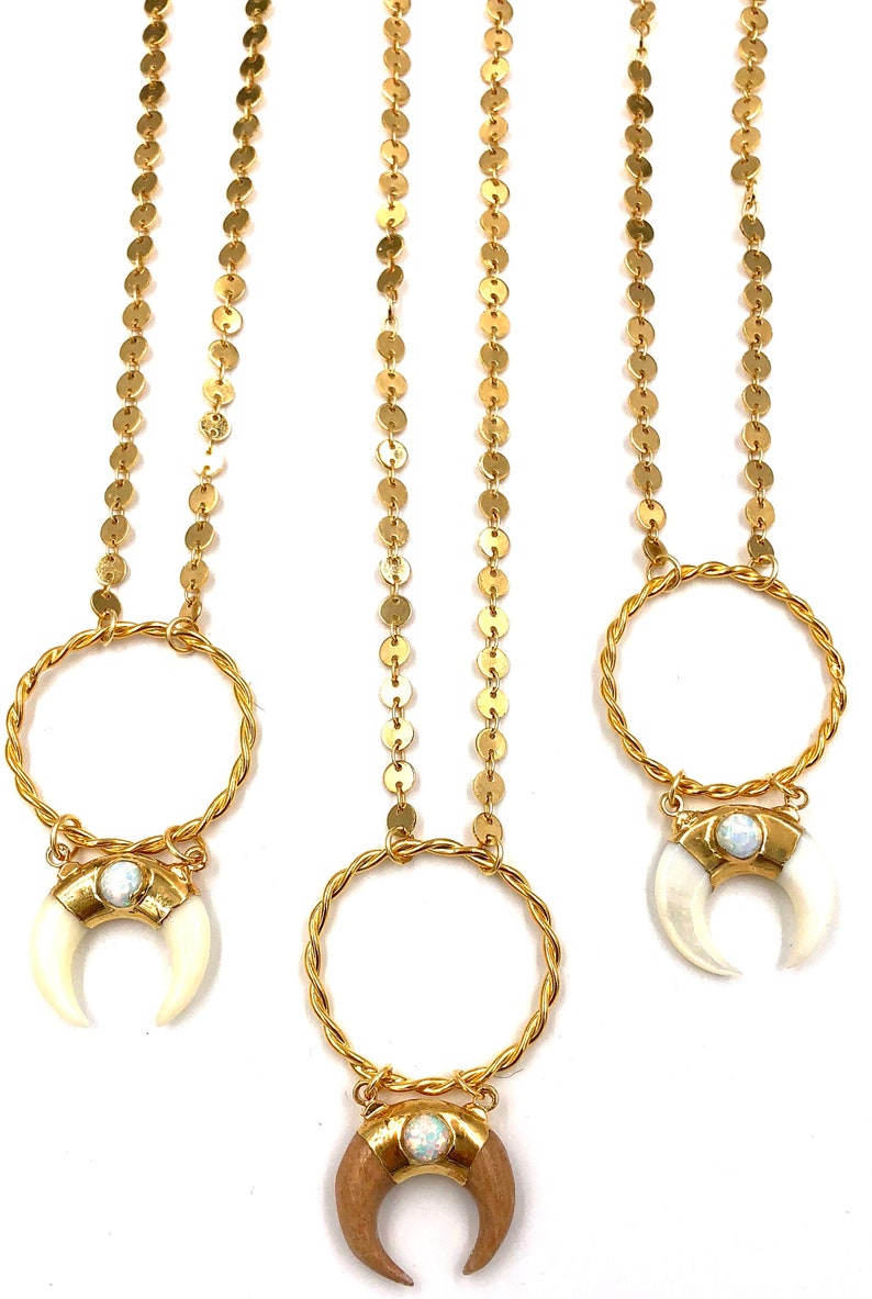 May include: Three gold necklaces with a crescent moon pendant. The pendants are made of wood, bone, and opal. The necklaces are made of gold chain and coin links.