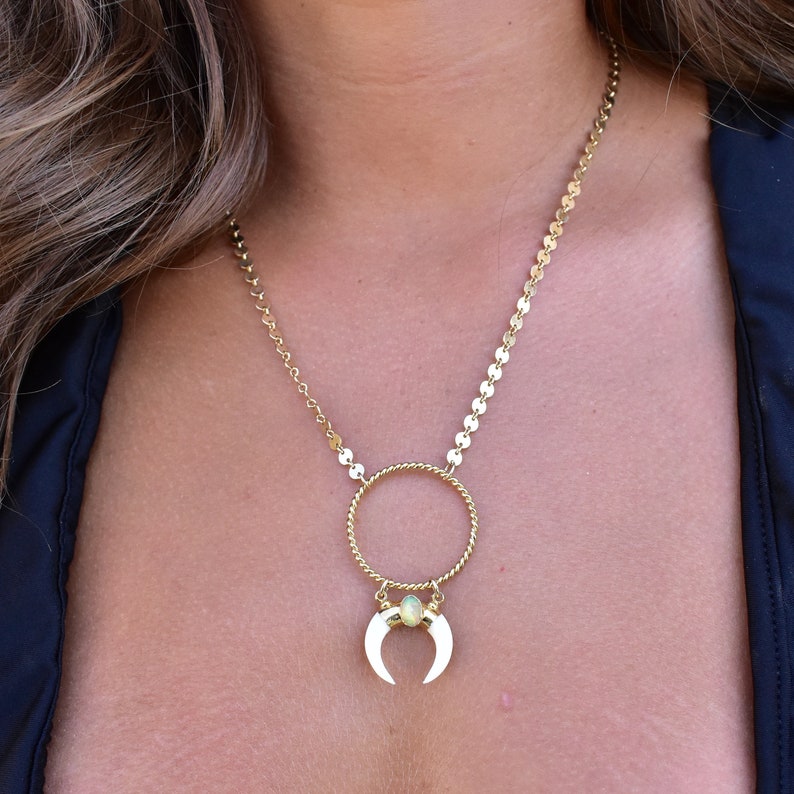 May include: A gold chain necklace with a circle pendant and a crescent moon charm with a green stone in the center.