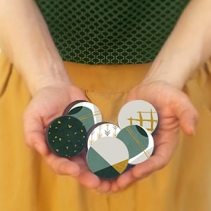 May include: A set of six round coasters with geometric patterns in shades of green, white, and gold. The coasters feature abstract designs with circles, lines, and arrows.