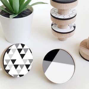 Op de afbeelding: Vier houten knoppen met verschillende geometrische patronen in zwart en wit. De knoppen zijn rond en hebben een vlak oppervlak. Ze zijn perfect om elke kamer een moderne uitstraling te geven.