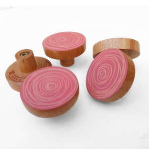 以下が含まれることがあります： ピンクの渦巻き模様が施された木製ノブが4つ。ノブの中央には真鍮製のネジがあり、1つのノブには「GALA」という文字が印刷されています。