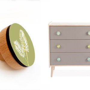 May include: A three-drawer dresser with a light gray finish and wooden legs. Each drawer has a round knob with a green and yellow floral design.