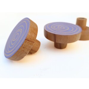 Puede incluir: Dos pomos de madera con un diseño de espiral morado y dorado. Los pomos son redondos y tienen un pequeño tallo en la parte inferior.