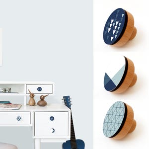 May include: Three wooden drawer knobs with different geometric patterns in shades of blue and white. The knobs are round and have a wood base.