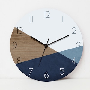 Peut inclure: Une horloge murale ronde, blanche, bleue et marron avec des aiguilles noires et des chiffres blancs. Le cadran de l'horloge est divisé en trois sections : une section blanche en haut, une section marron à gauche et une section bleue à droite.