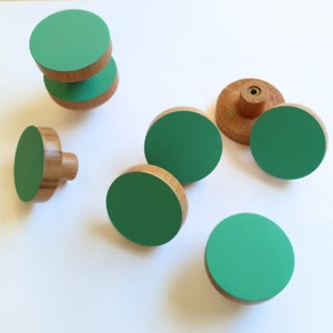 K&ouml;nnte beinhalten: Satz mit sechs runden Schrankkn&ouml;pfen in Gr&uuml;n und Holz. Die Kn&ouml;pfe sind aus Holz mit einer gr&uuml;n lackierten Oberseite.