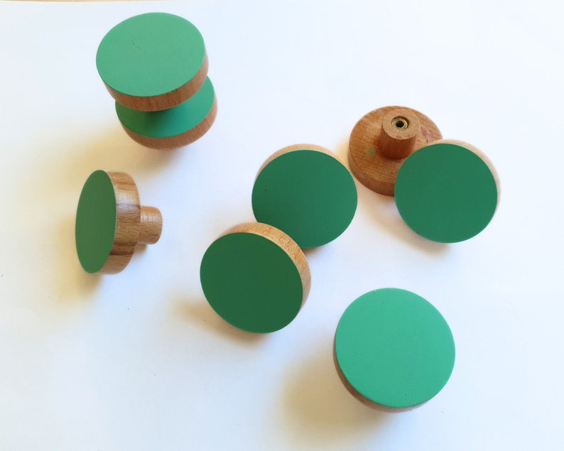 K&ouml;nnte beinhalten: Satz mit sechs runden Schrankkn&ouml;pfen in Gr&uuml;n und Holz. Die Kn&ouml;pfe sind aus Holz mit einer gr&uuml;n lackierten Oberseite.
