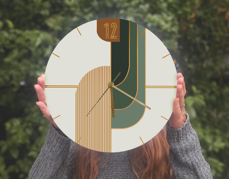 May include: A white round clock with gold and green geometric shapes and gold hands. The clock face has the number "12" in a gold rectangle.