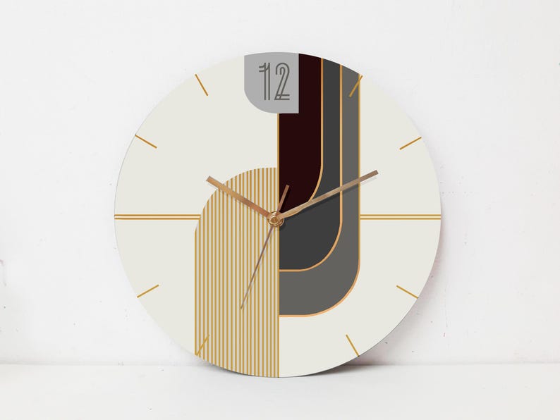 May include: White round clock with gold hands and a geometric design featuring black, gray, and gold stripes. The clock face has the number "12" printed on it.