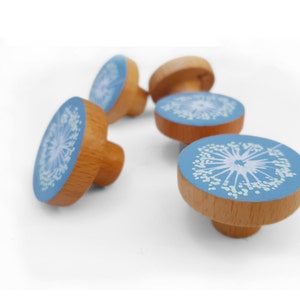 May include: Set of four wooden knobs with a blue and white dandelion design. The knobs are round and have a raised edge. They are perfect for adding a touch of whimsy to any room.