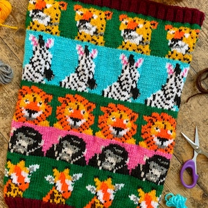 Peut inclure: Un col tricoté avec un motif répété de visages d'animaux. Le motif comprend des tigres, des zèbres, des lions, des gorilles et des girafes aux couleurs vives comme l'orange, le vert, le rose et le bleu. Le col a une bordure côtelée bordeaux.