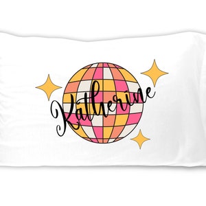 May include: White pillowcase with a pink and orange disco ball design and the name "Katherine" written in black cursive.