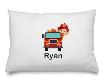 May include: White rectangular pillow with a cartoon illustration of a red fire truck and a firefighter. The firefighter is wearing a red helmet and waving. The name "Ryan" is printed in black below the fire truck.
