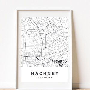 May include: A framed black and white map print of Hackney, London. The print features a detailed street map with the name "HACKNEY" and coordinates 51.5436°N 0.0554°W at the bottom. The map is encased in a white frame.
