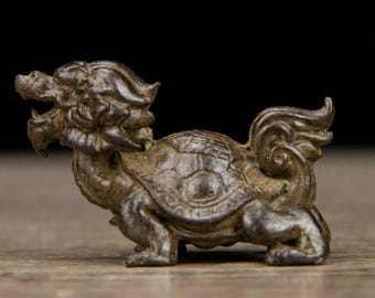 May include: A bronze-colored figurine depicting a mythical creature. The figure has a dragon-like head, a turtle shell, and a curled tail. The sculpture is detailed and appears to be made of metal.