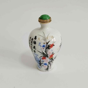 May include: A white ceramic bottle with a green stopper and gold trim. The bottle is decorated with a floral and bird design in red, blue, and black, with Chinese characters.