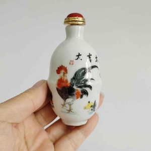 May include: A white ceramic bottle with a red and gold stopper. The bottle features a hand-painted rooster design in red, black, and yellow, with Chinese characters. A decorative item.